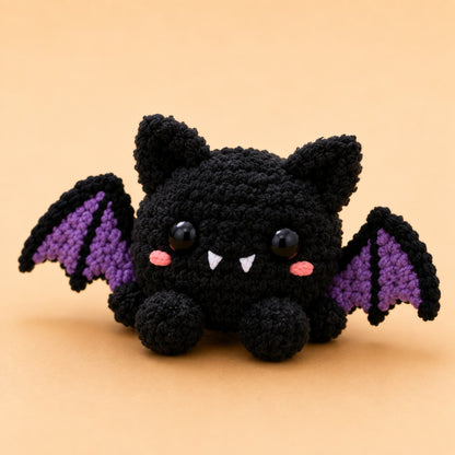Handmade crochet black bat plush with purple wings, tiny fangs and pink blushed cheeks
