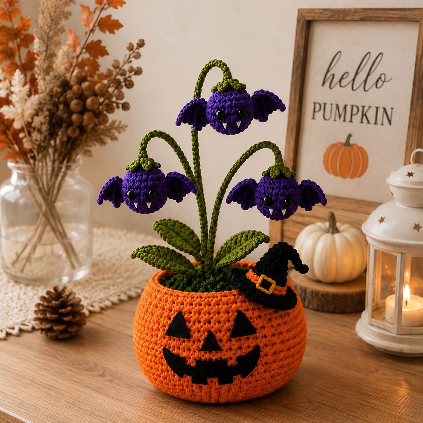Handmade crochet pumpkin flower pot holding purple bat blooms with fangs beside a black witch hat