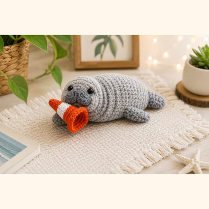 Grey crochet seal plush styled on a fringed rug with houseplants and fairy lights