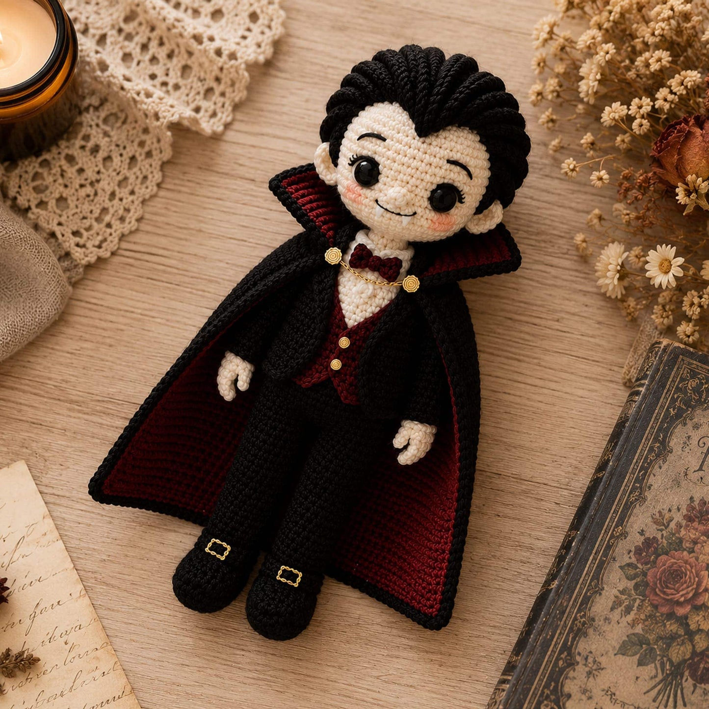 Flat lay of a handmade crochet Dracula doll beside a candle, dried roses and an antique book