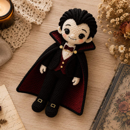 Flat lay of a handmade crochet Dracula doll beside a candle, dried roses and an antique book